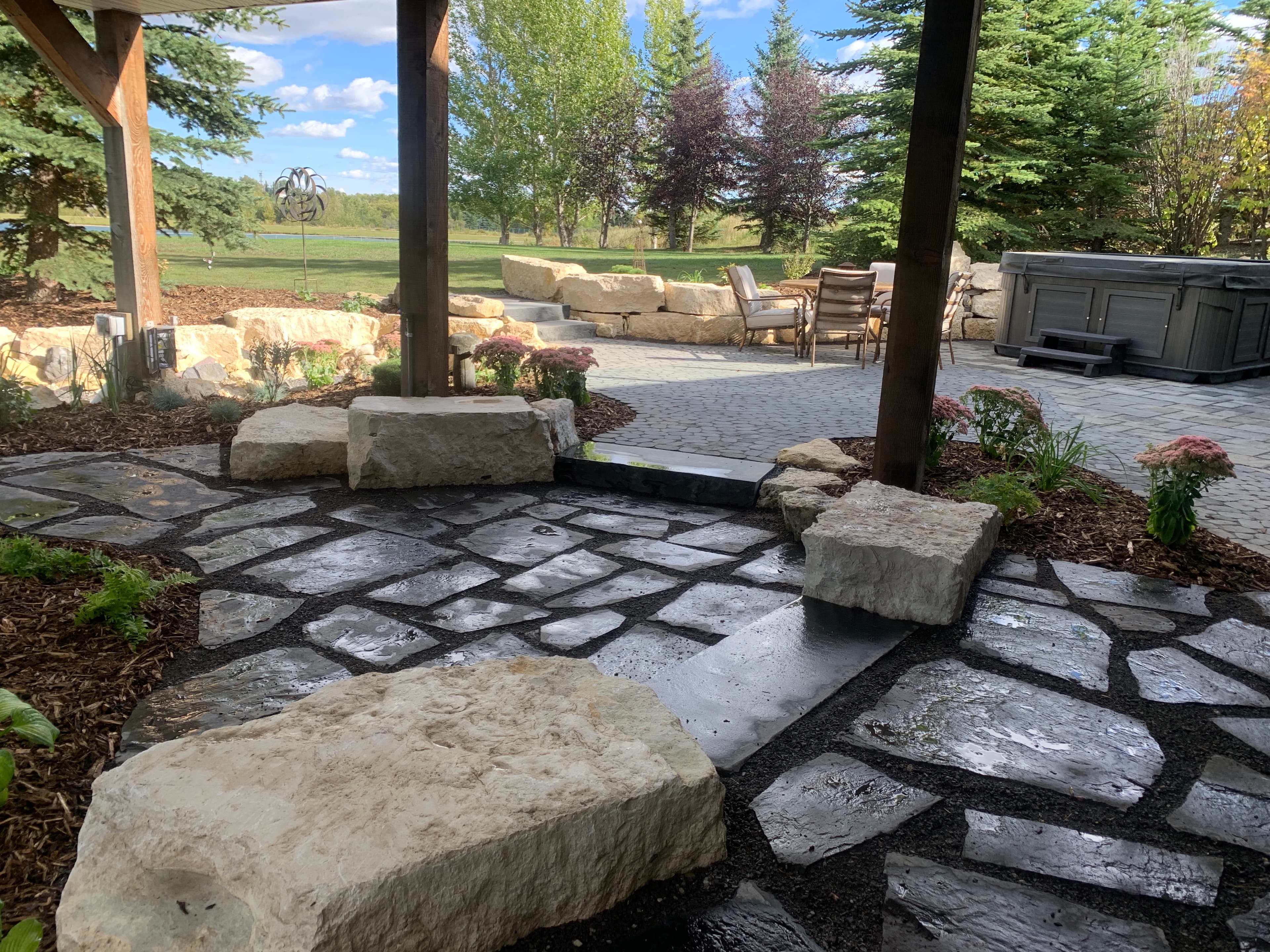 Landscaped backyard with flagstone path, large stone blocks, patio furniture, and a hot tub.