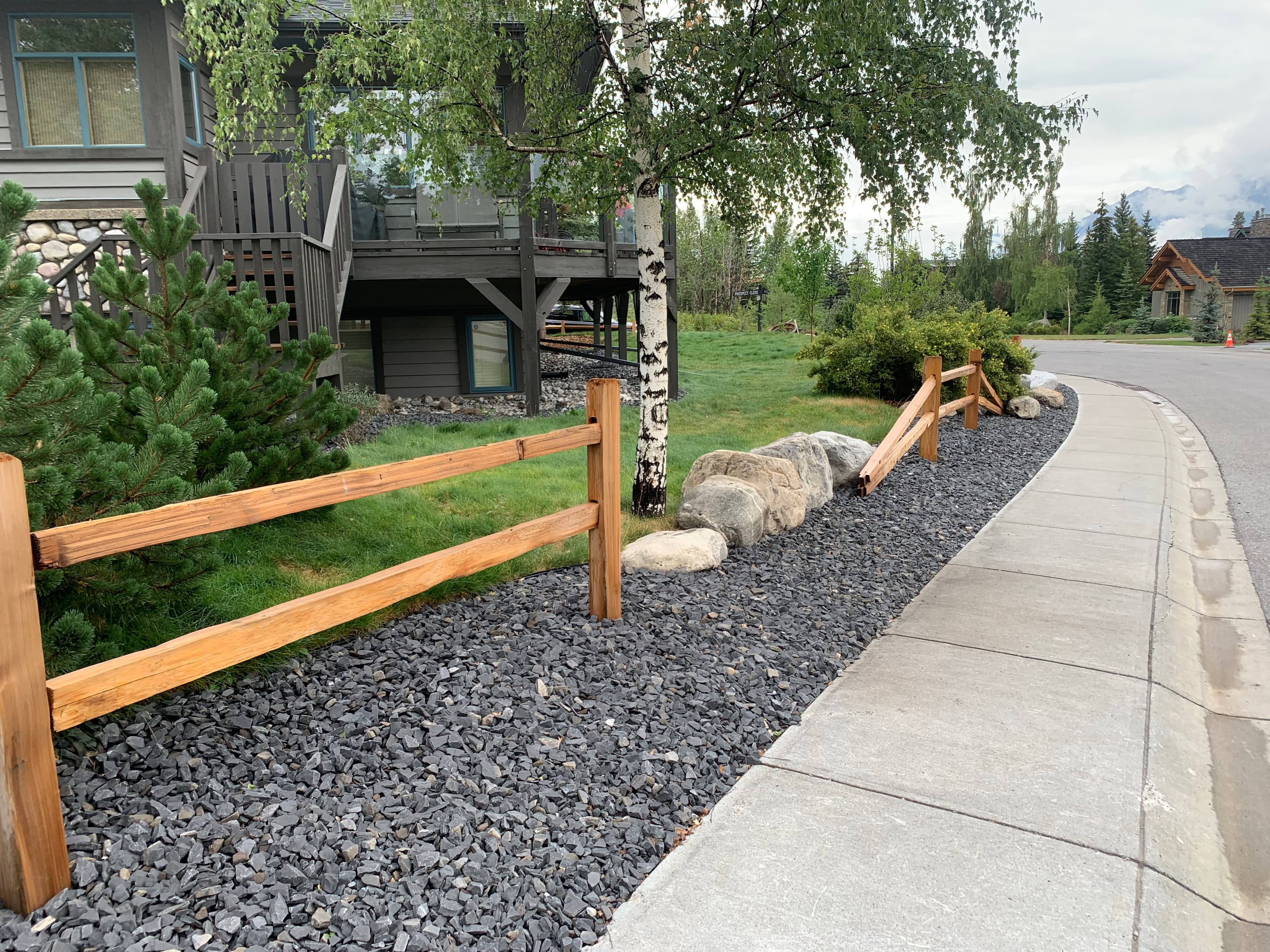 Split-rail wooden fence along a gravel path and sidewalk in a landscaped residential yard.