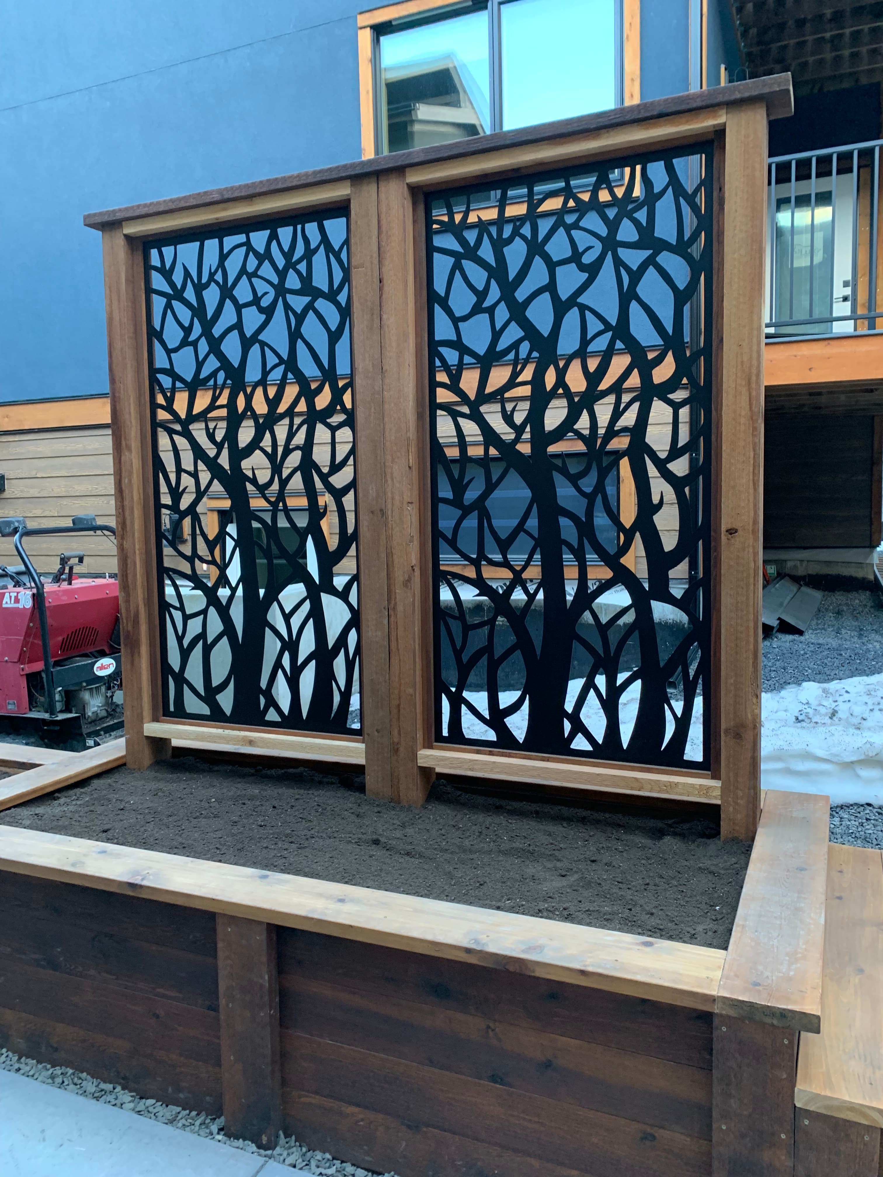 Wooden privacy screen with decorative black metal branch-patterned panels and an attached wooden planter box.