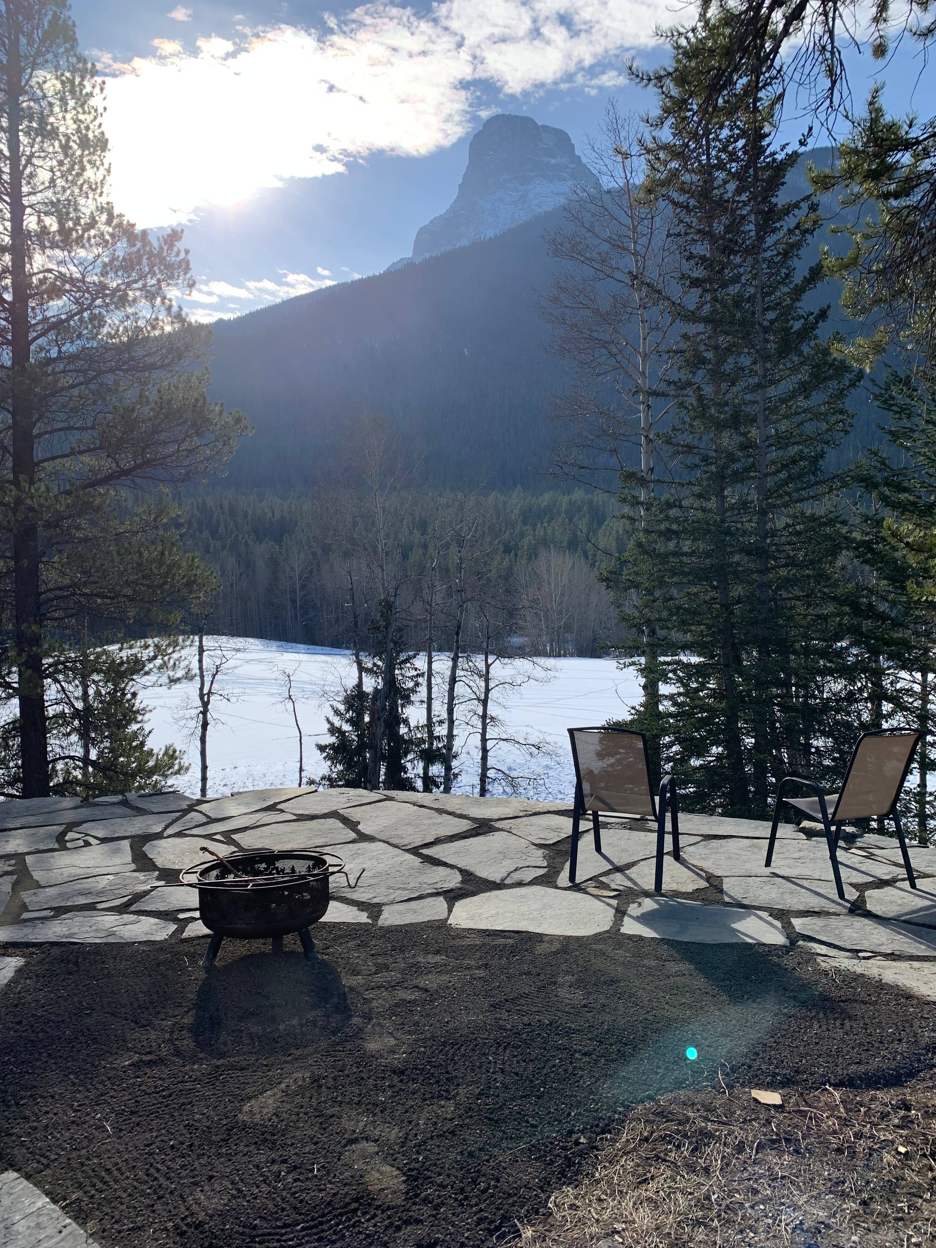 Stone patio with chairs and fire pit overlooking a scenic mountain and forest landscape.