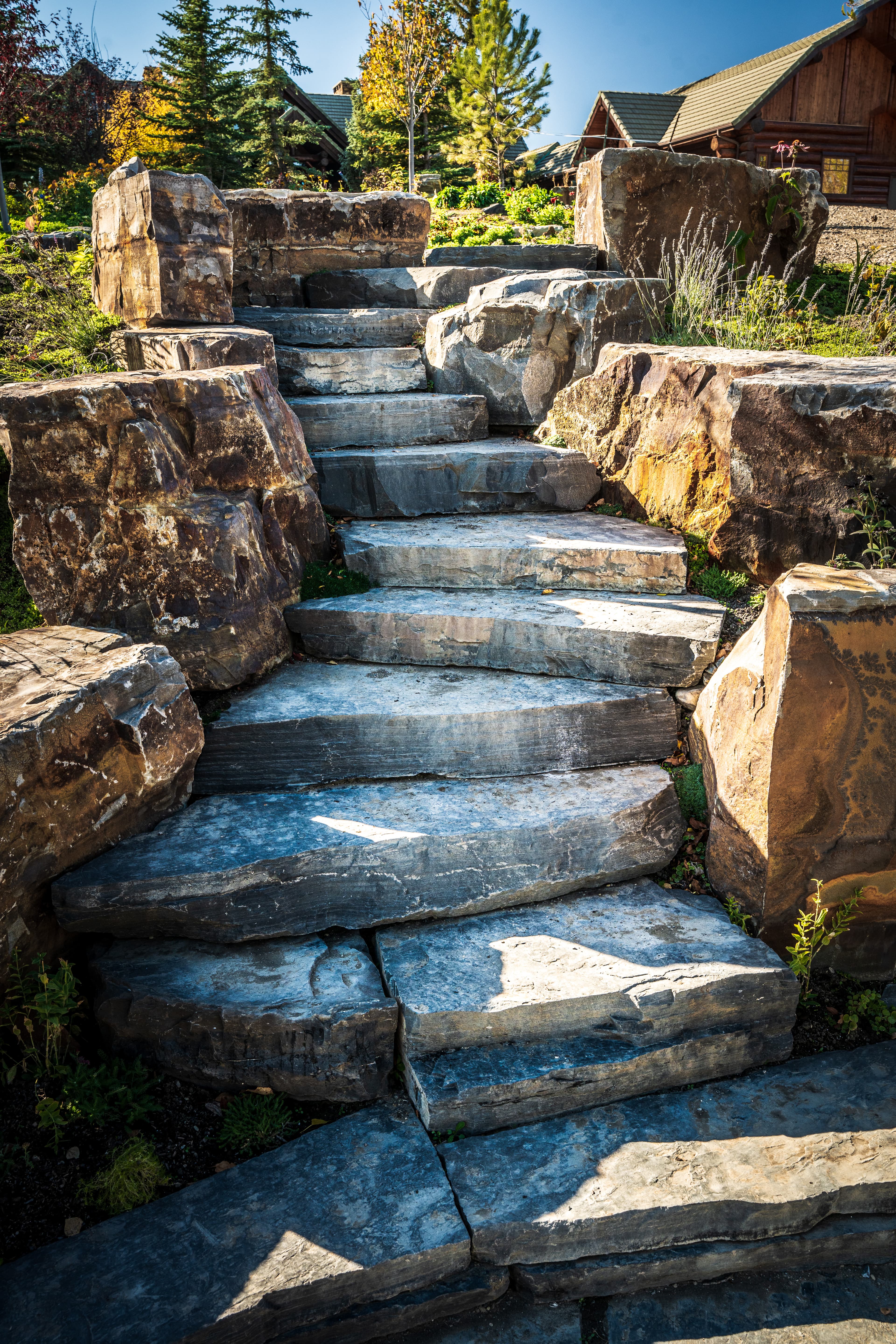 Large flat grey stone steps winding up a hillside between boulders toward a cabin.