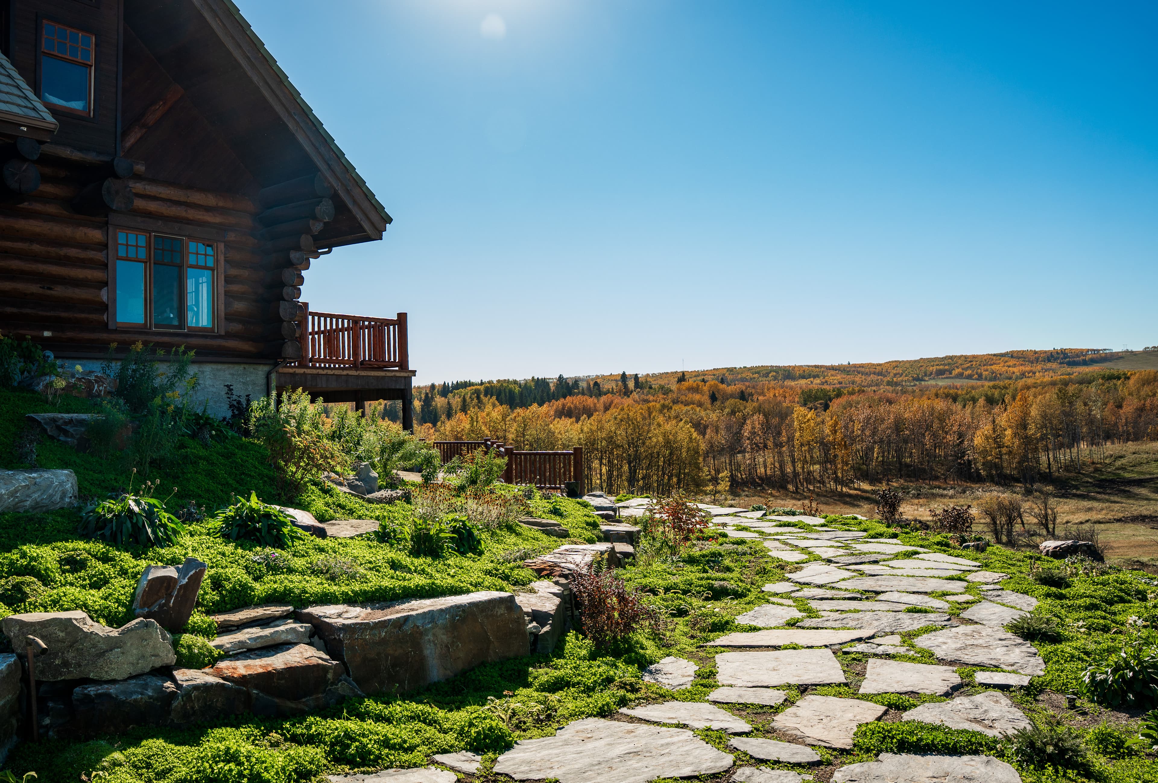 Rustic log cabin overlooking a stone path and a forest of golden autumn trees.