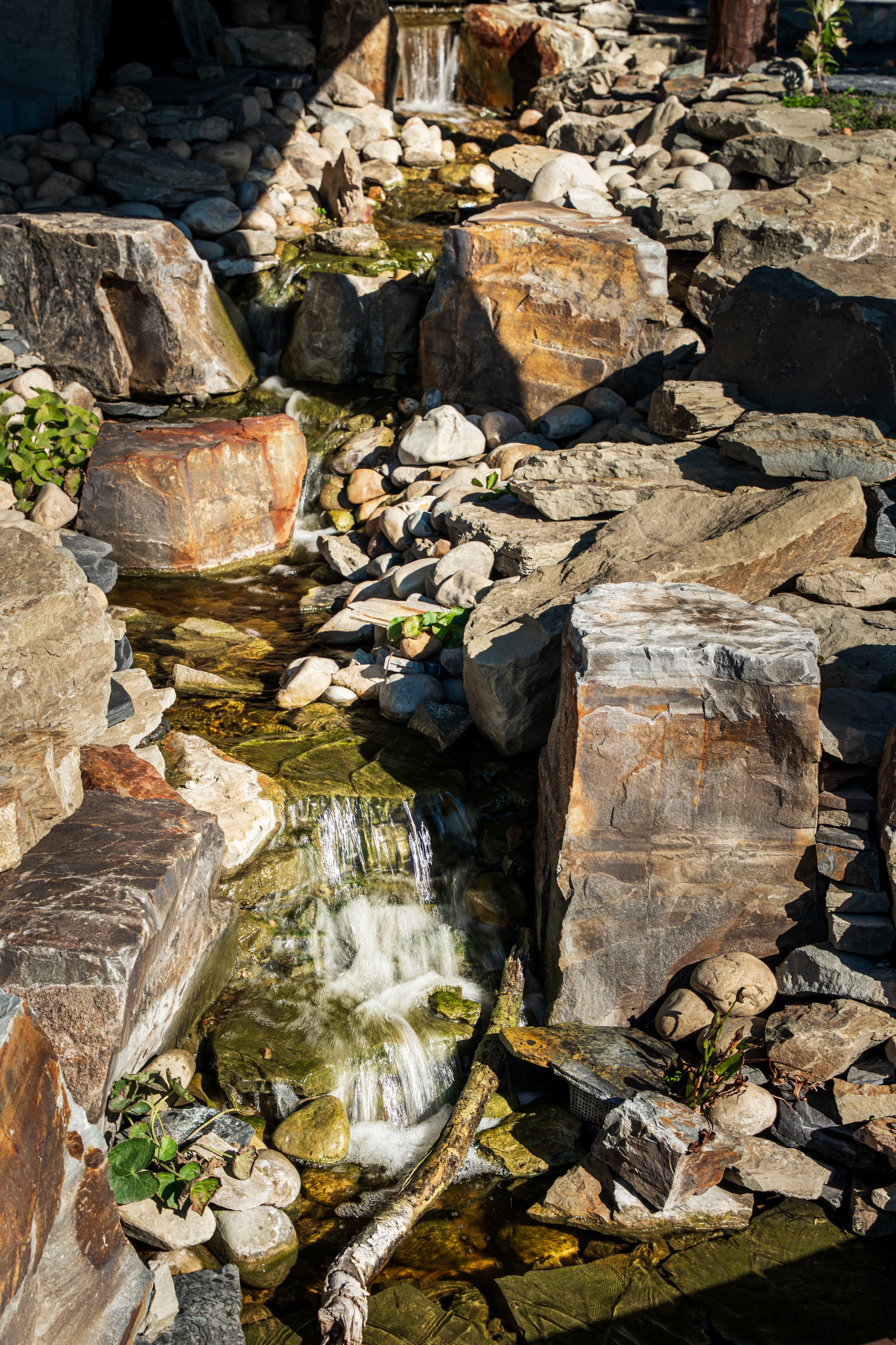 A small rocky stream with water cascading over stones and pebbles in bright sunlight.