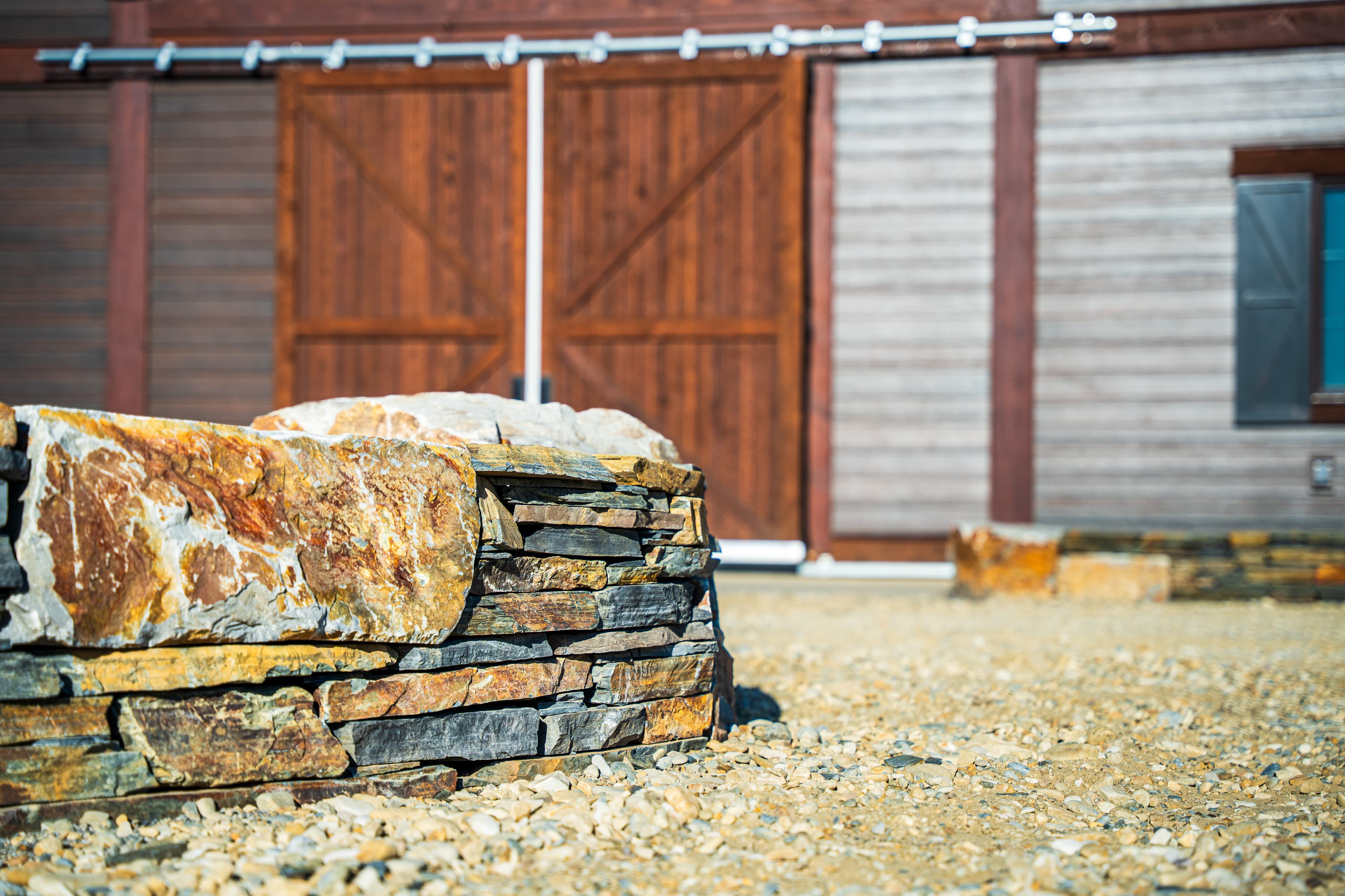 Stacked natural stone wall on gravel in front of a blurred rustic wooden barn.